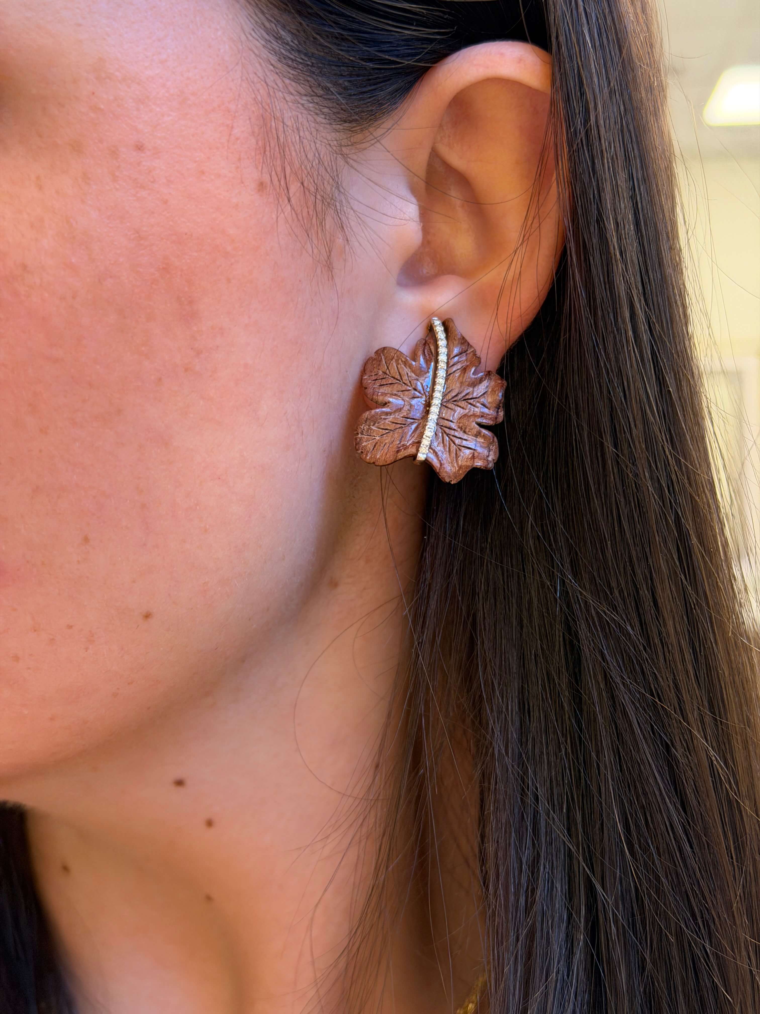 Close-up of an ear wearing a leaf-shaped earring with a blurred background