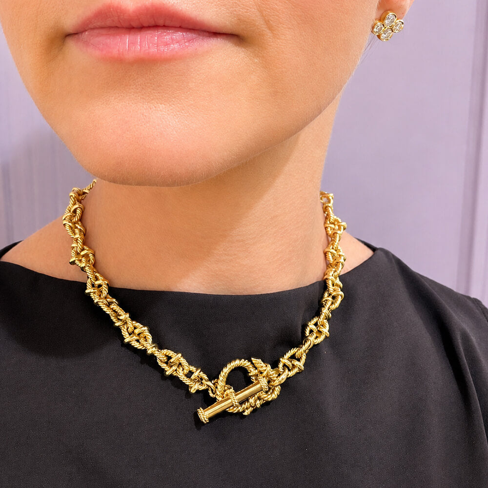 A close-up of a model wearing a chunky 18K yellow gold chain necklace with a toggle clasp 