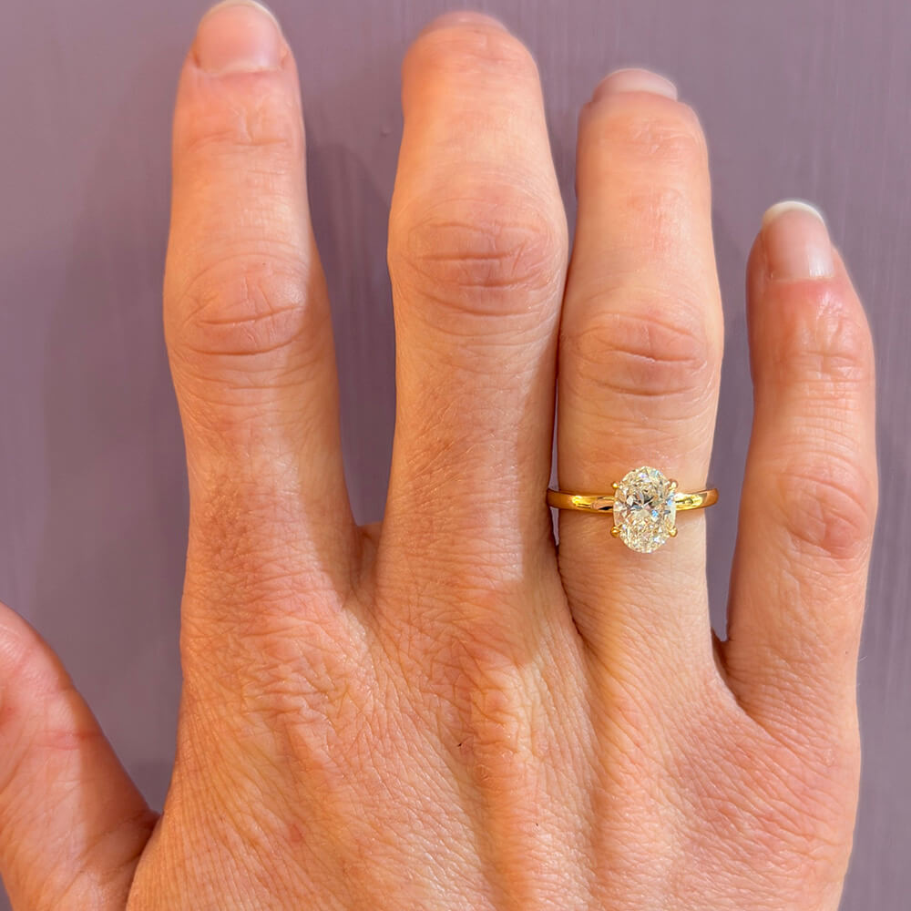18K Gold ring with a diamond on a woman's finger against a plain background