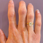 18K Gold ring with a diamond on a woman's finger against a plain background