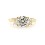 A custom designed round brilliant diamond ring with trapezoid side diamonds in hammered 18K yellow gold