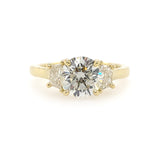 A custom designed round brilliant diamond ring with trapezoid side diamonds in hammered 18K yellow gold