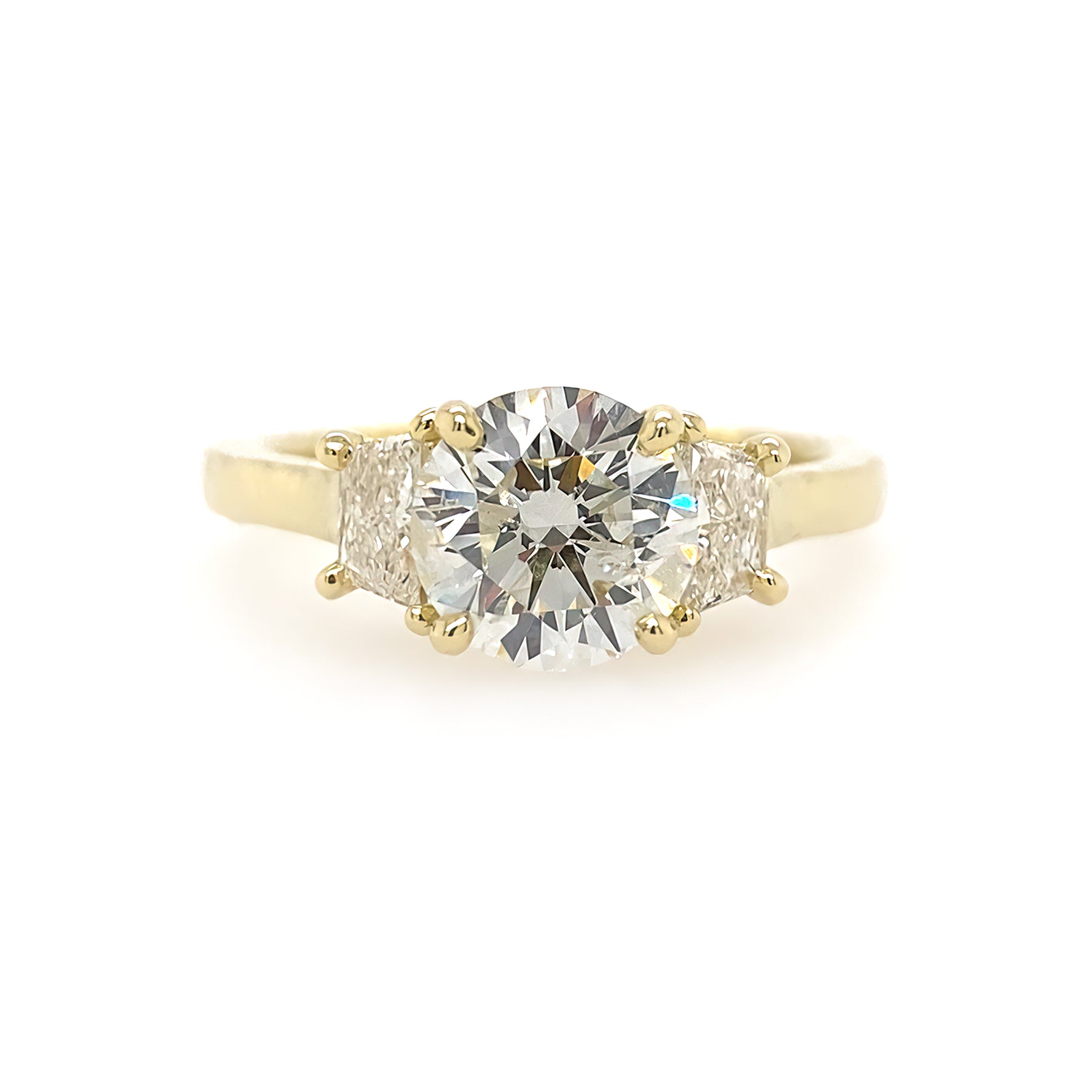 A custom designed round brilliant diamond ring with trapezoid side diamonds in hammered 18K yellow gold