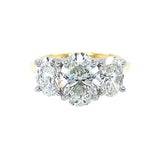 A three-stone diamond ring featuring a central oval brilliant-cut diamond flanked by two oval-cut diamonds, set in an 18K yellow gold band with platinum prongs, isolated on a white background.