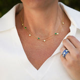 woman wearing an 18k yellow gold necklace with green emerald gemstones and a white shirt.