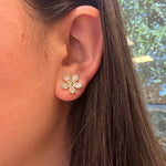 Close-up of a woman's ear wearing an 18K gold and diamond flower earring with a blurred background