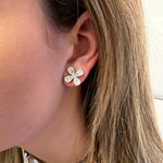 A close-up of a woman's ear wearing a four-petal flower stud earring with sparkling diamonds