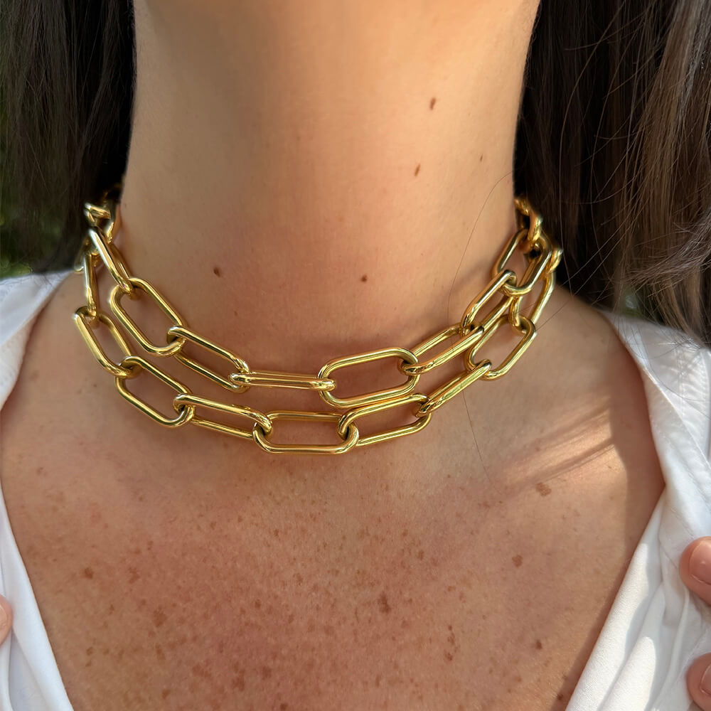 A close-up of a woman's neck and upper chest wearing a chunky, double-layered gold chain choker necklace.