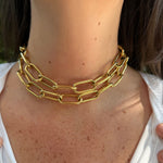 A close-up of a woman's neck and upper chest wearing a chunky, double-layered gold chain choker necklace.