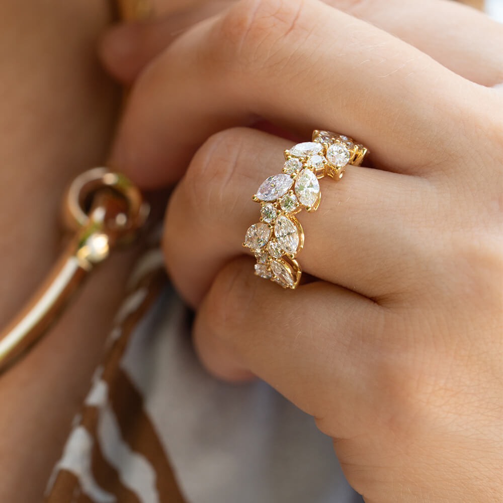 A close-up of an 18K yellow gold ring featuring a row of marquise-cut clear diamonds, worn on a finger. 