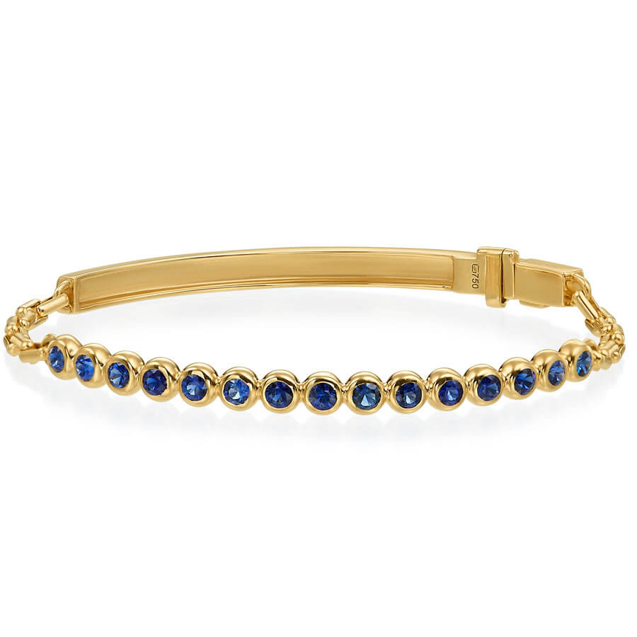 A yellow gold bangle bracelet featuring a row of round-cut deep blue sapphires, displayed on a clean white background.