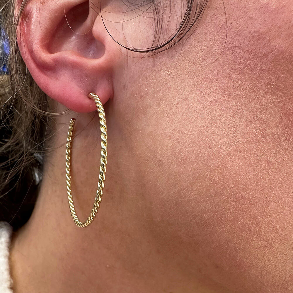 A close-up of a woman's ear wearing a gold hoop earring with a twisted rope texture.