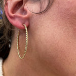 A close-up of a woman's ear wearing a gold hoop earring with a twisted rope texture.