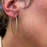A close-up of a woman's ear wearing a gold hoop earring with a twisted rope texture.