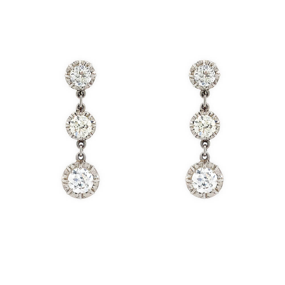 A pair of 18K white gold drop earrings, each featuring three graduated round-cut clear diamonds, shown against a plain white background.