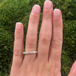 Hand wearing an 18K gold ring with emerald cut diamondsa green mossy background