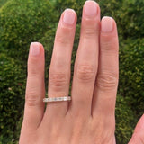 Hand wearing an 18K gold ring with emerald cut diamondsa green mossy background
