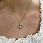 18K Gold necklace with a clover-shaped pendant with a diamond on a woman wearing a white dress.