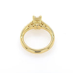 An 18K yellow gold ring with a decorative filigree band and a central radiant-cut diamond, shown from a top-down view on a white background.