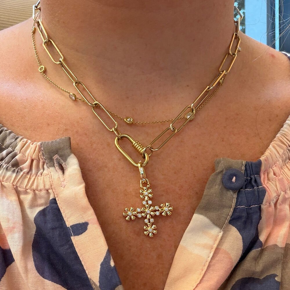 A close-up of a woman wearing an 18k yellow gold small Fiori Cross pendant with diamonds designed by Temple St. Clair  