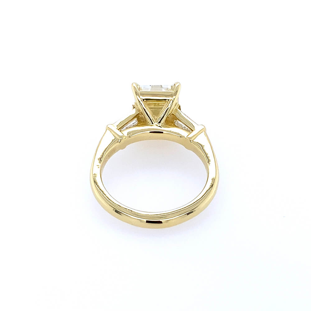 An 18K yellow gold ring with a triangular prong setting holding a clear rectangular diamond, shown on a plain white background.