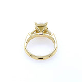 An 18K yellow gold ring with a triangular prong setting holding a clear rectangular diamond, shown on a plain white background.