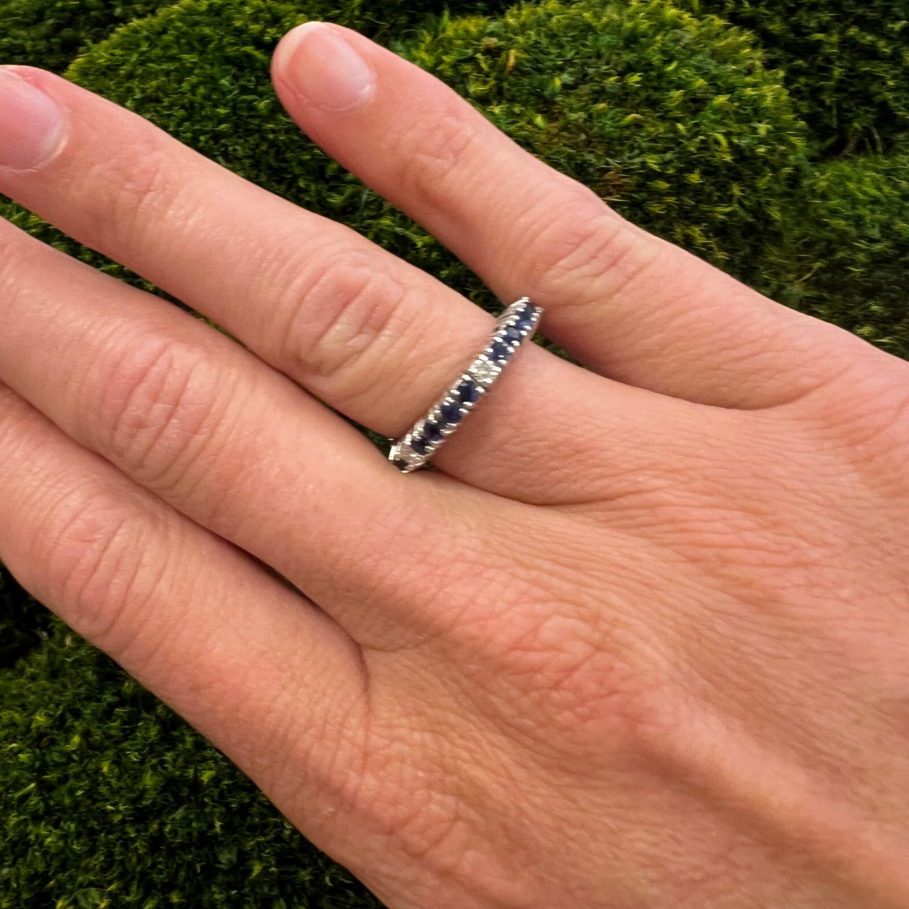 A woman's hand wearing a white gold eternity band ring with diamonds and sapphires