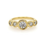 A golden 18k yellow gold bezel set diamond band ring with multiple small clear diamonds around the main large diamond.