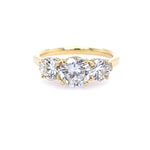 An 18k yellow gold three stone round diamond ring with a gold band and a central diamond surrounded by smaller round diamonds.