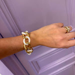 Hand wearing a gold and white chain bracelet against a purple background