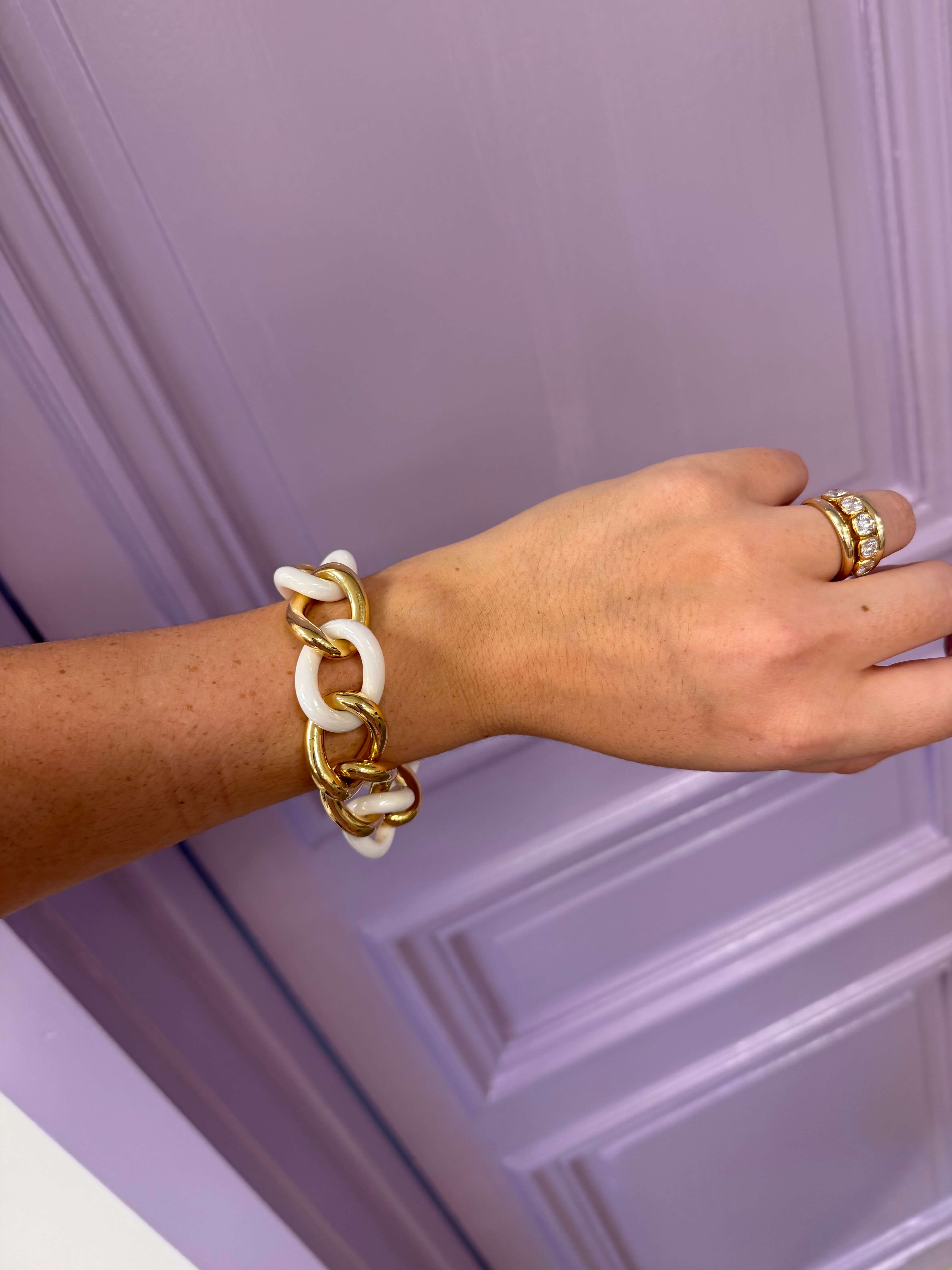 Hand wearing a gold and white chain bracelet against a purple background