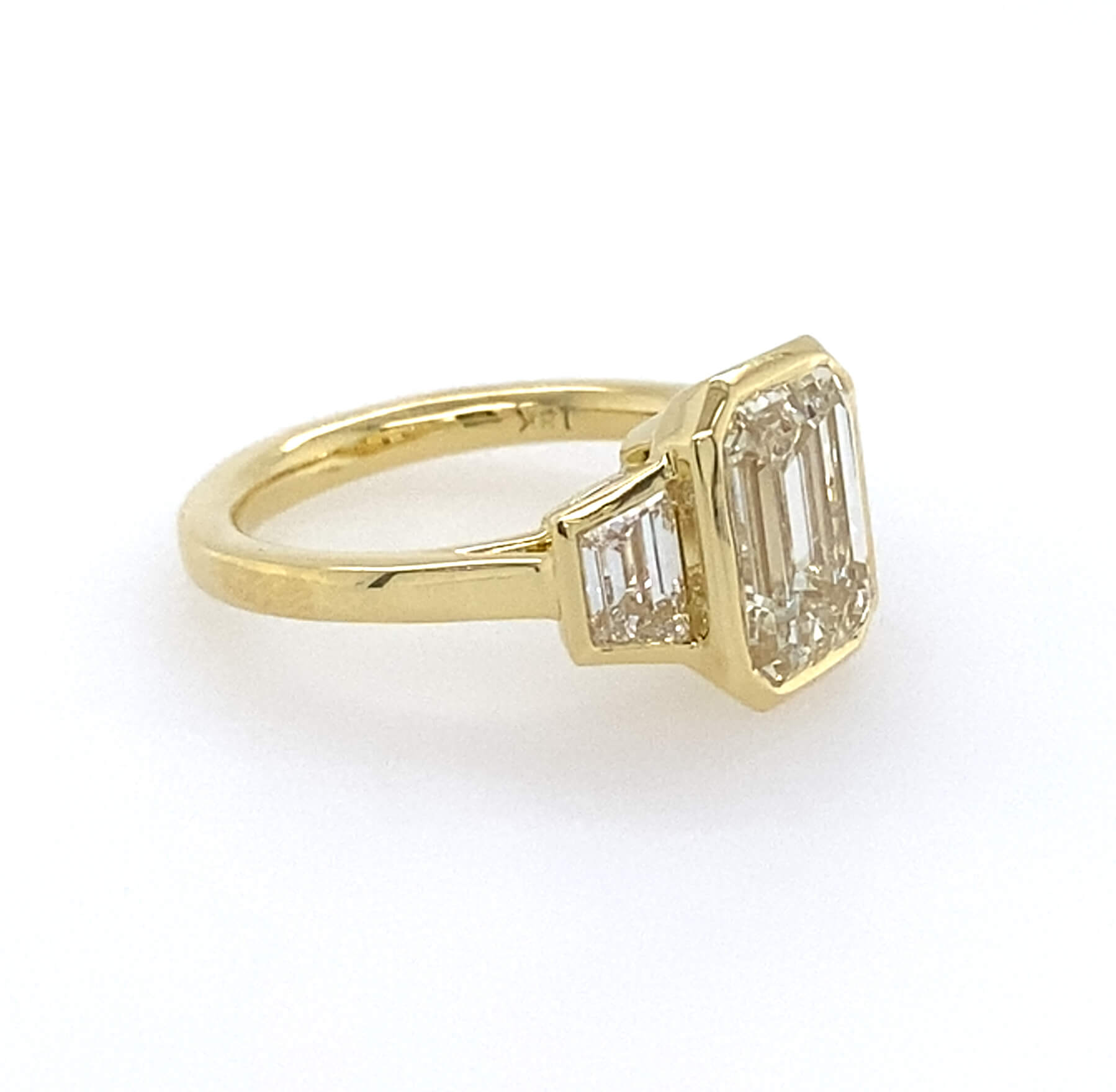 Side View 18k yellow gold bezel set emerald cut engagement ring with trapezoids side stones 