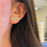 Close-up of an ear wearing a gold earring with small stones.