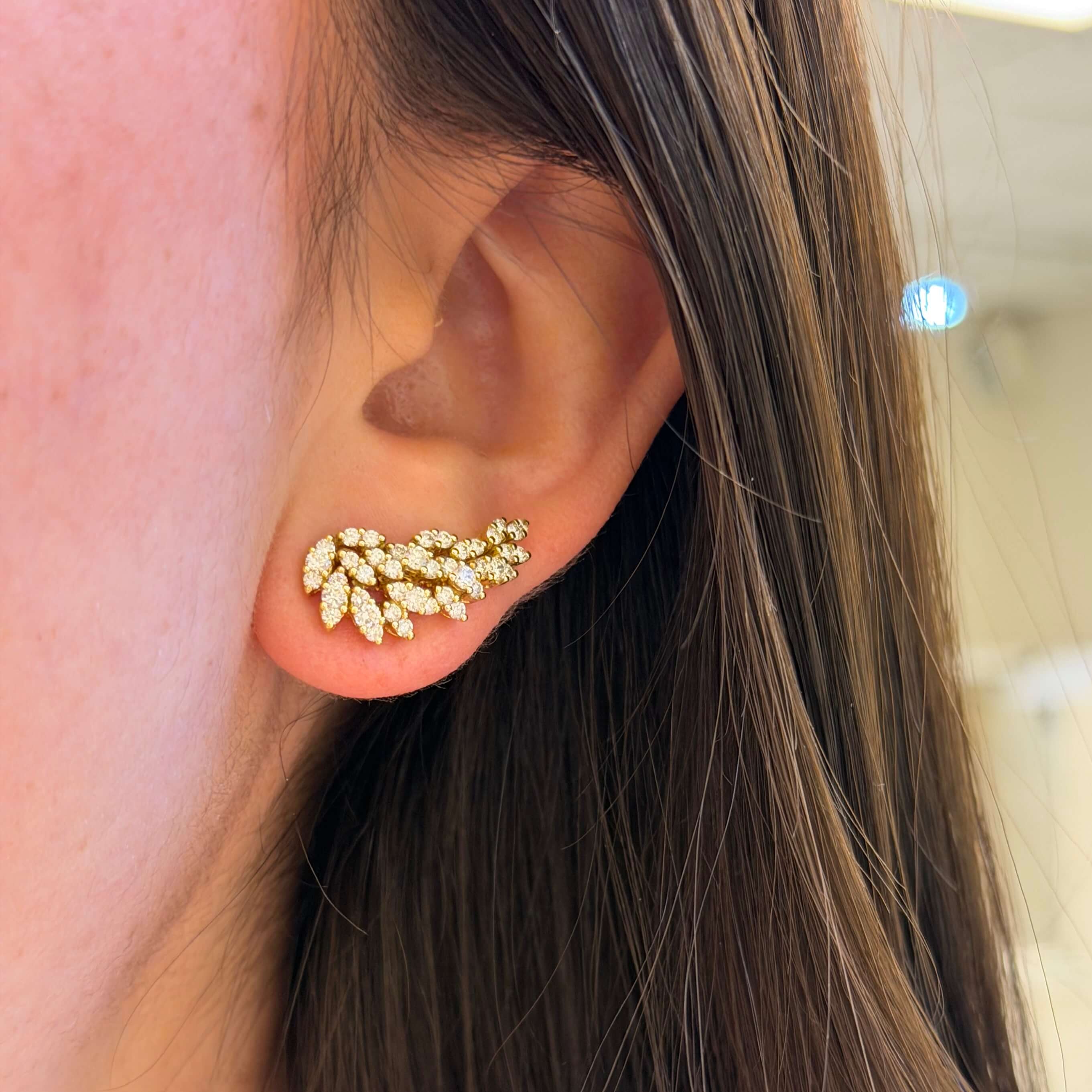 Close-up of a woman wearing an 18K gold diamond earring shaped like leafs