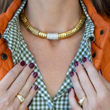 Close-up of a person wearing a gold necklace with a green checkered shirt and orange jacket.