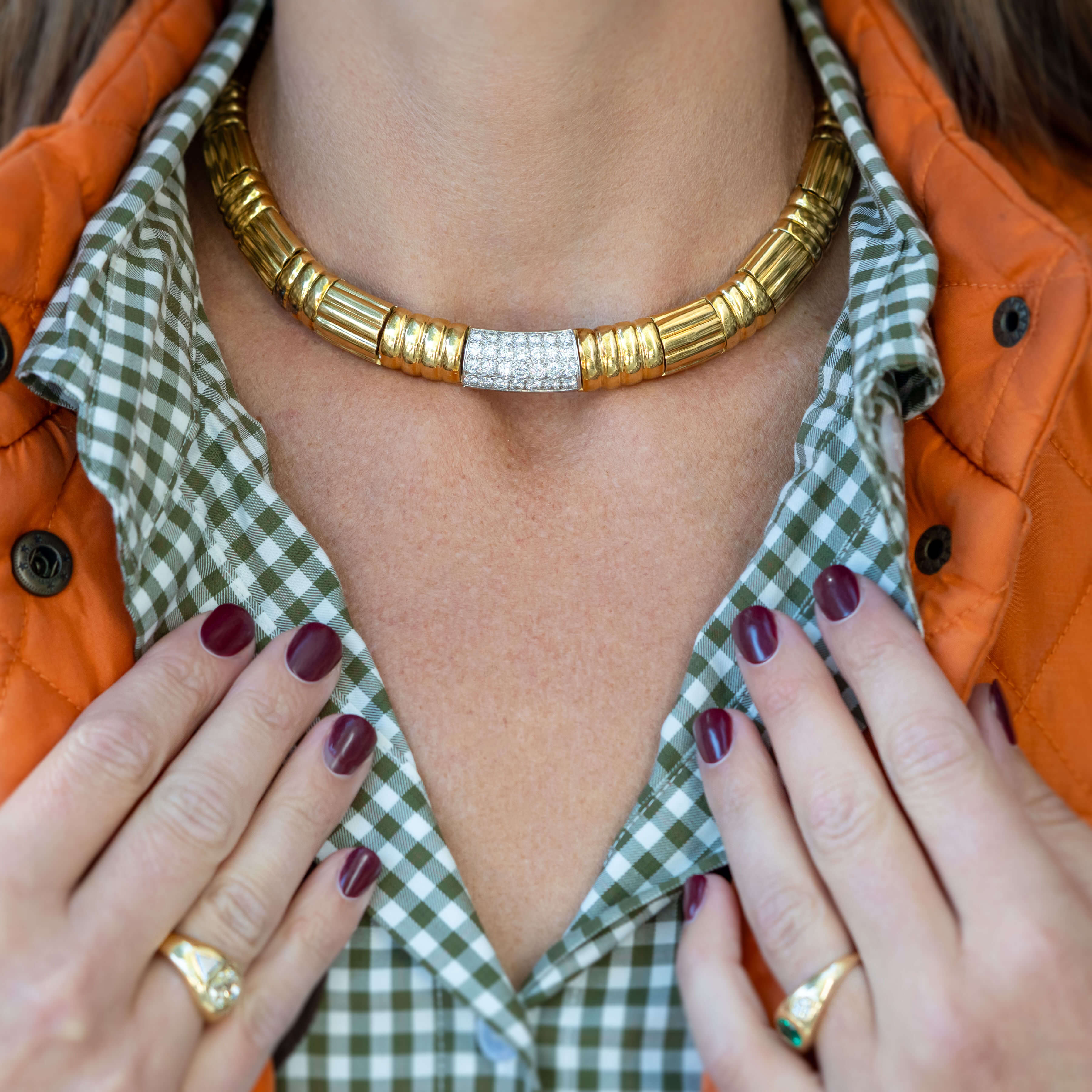 Close-up of a person wearing a gold necklace with a green checkered shirt and orange jacket.