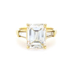 18K yellow gold ring with a large emerald-cut diamond and smaller baguette diamonds on a white background