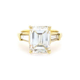 18K yellow gold ring with a large emerald-cut diamond and smaller baguette diamonds on a white background