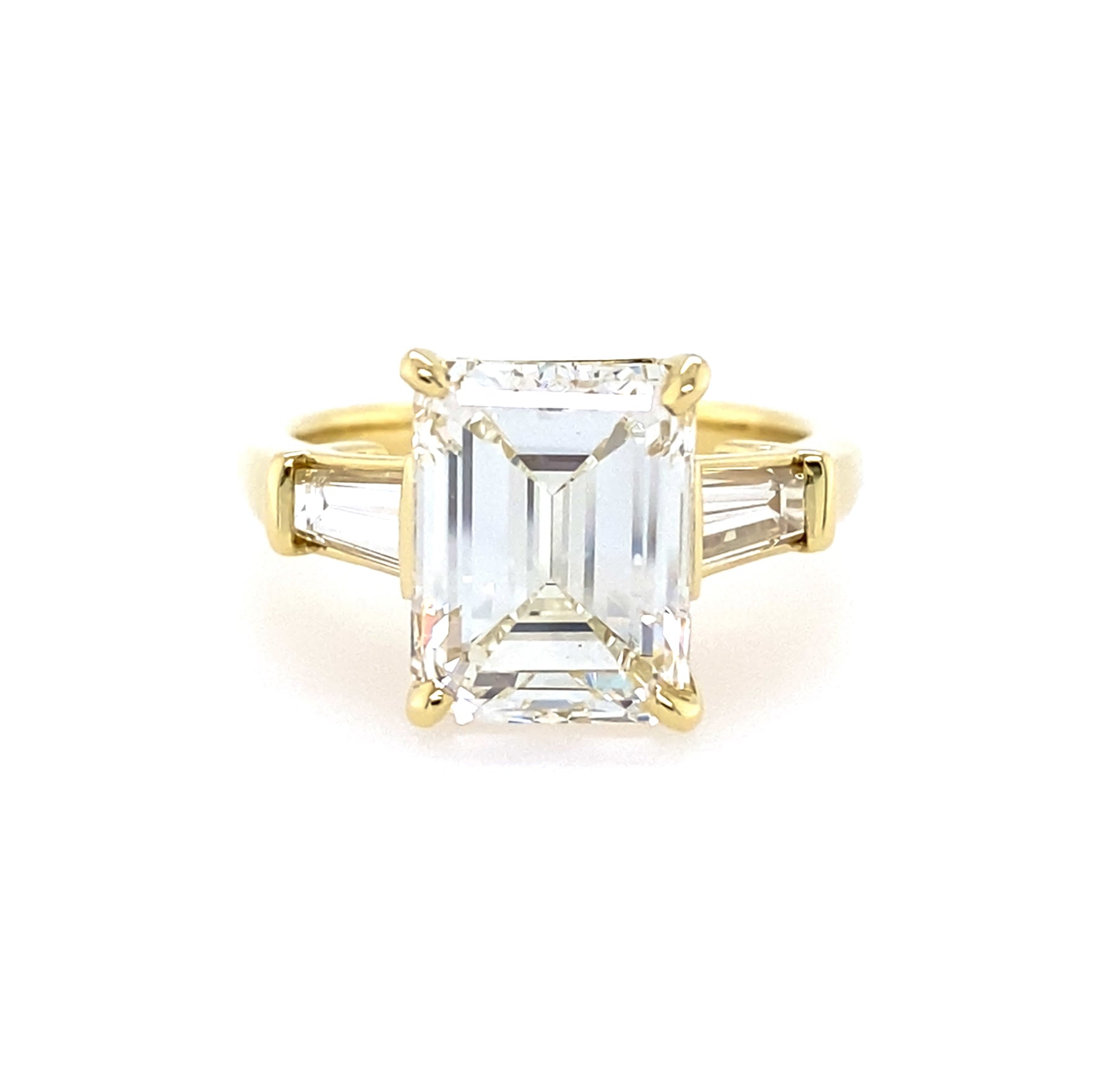 18K yellow gold ring with a large emerald-cut diamond and smaller baguette diamonds on a white background