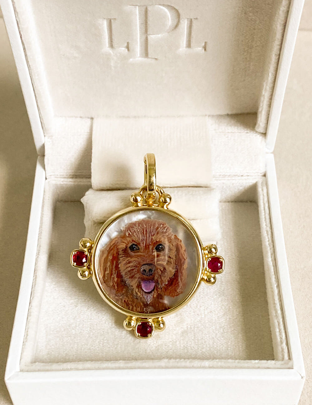 A round gold pendant featuring a custom portrait of a brown dog, displayed inside an open white jewelry box with the brand name 'LPL' embossed on the inside lid.