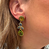 A close-up of a woman's ear wearing a 22k gold  earring with green peridot gemstone accents and small aquamarine stones.
