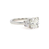 A three-stone diamond engagement ring featuring a cushion-cut center diamond and two half moon side diamonds in a platinum metal band, set against a plain white background.