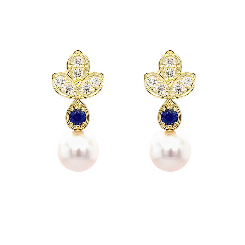 A pair of 18K yellow gold leaf-shaped stud earrings with six diamonds each and a round deep blue sapphire, and a dangling white pearl, shown on a plain white background.