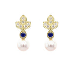 A pair of 18K yellow gold leaf-shaped stud earrings with six diamonds each and a round deep blue sapphire, and a dangling white pearl, shown on a plain white background.