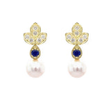 A pair of 18K yellow gold leaf-shaped stud earrings with six diamonds each and a round deep blue sapphire, and a dangling white pearl, shown on a plain white background.