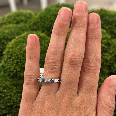 Hand wearing a ring with sapphire and diamond gemstones against a blurred green background