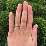 Hand wearing a platinum ring with emerald gemstones and diamonds against a green background