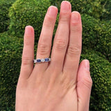 Hand wearing a platinum ring with sapphire and diamond stones against a green bush background