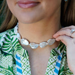 Close-up of a woman wearing a Baroque pearl necklace with a green and white patterned top.