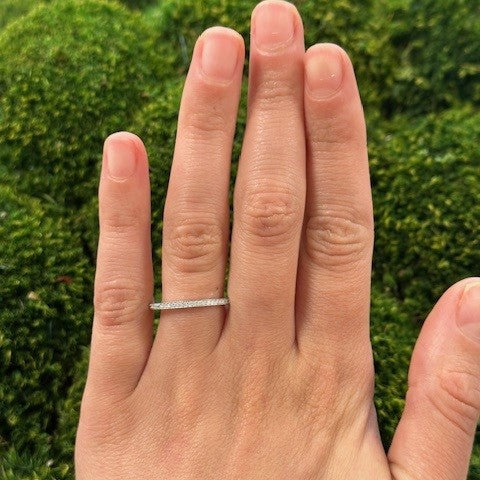 Hand wearing a platinum ring with diamonds against a green blurred background